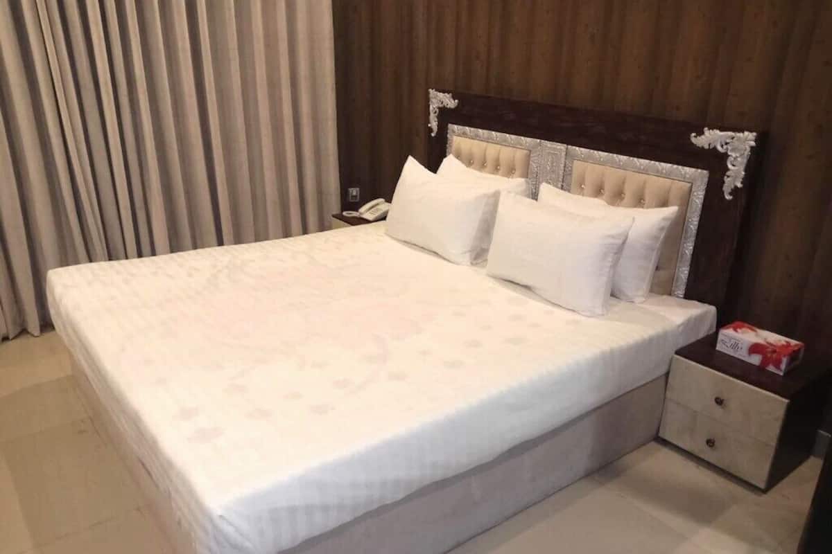 A neatly made bed with a wooden headboard, a bedside table with a phone, and a nightstand with a box.