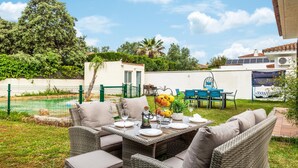 An outdoor dining area with wicker furniture, a table set for four, and a view of a swimming pool and greenery in the background. - Beautiful home in Bollullos de la Mitaci (Bollullos de la Mitaci)