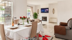 A dining area with a table set for four, a television mounted on the wall, and a fireplace in the background. - Beautiful home in Bollullos de la Mitaci (Bollullos de la Mitaci)