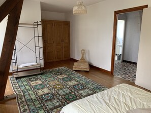 A bedroom with a bed, a patterned rug, a wooden wardrobe, and a hanging light fixture.