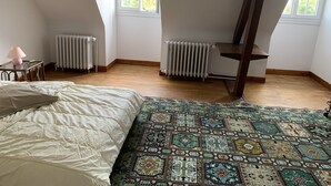 A bedroom with a large bed, a patterned rug, two radiators, and a window with a view of trees.
