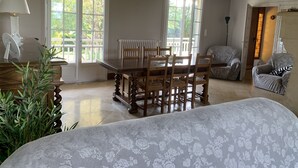 A dining area with a wooden table and chairs, large windows, a radiator, and a sofa.