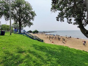 Une plage avec une zone herbeuse qui mène à une plage de sable, un escalier et une jetée qui s’avance dans l’eau.