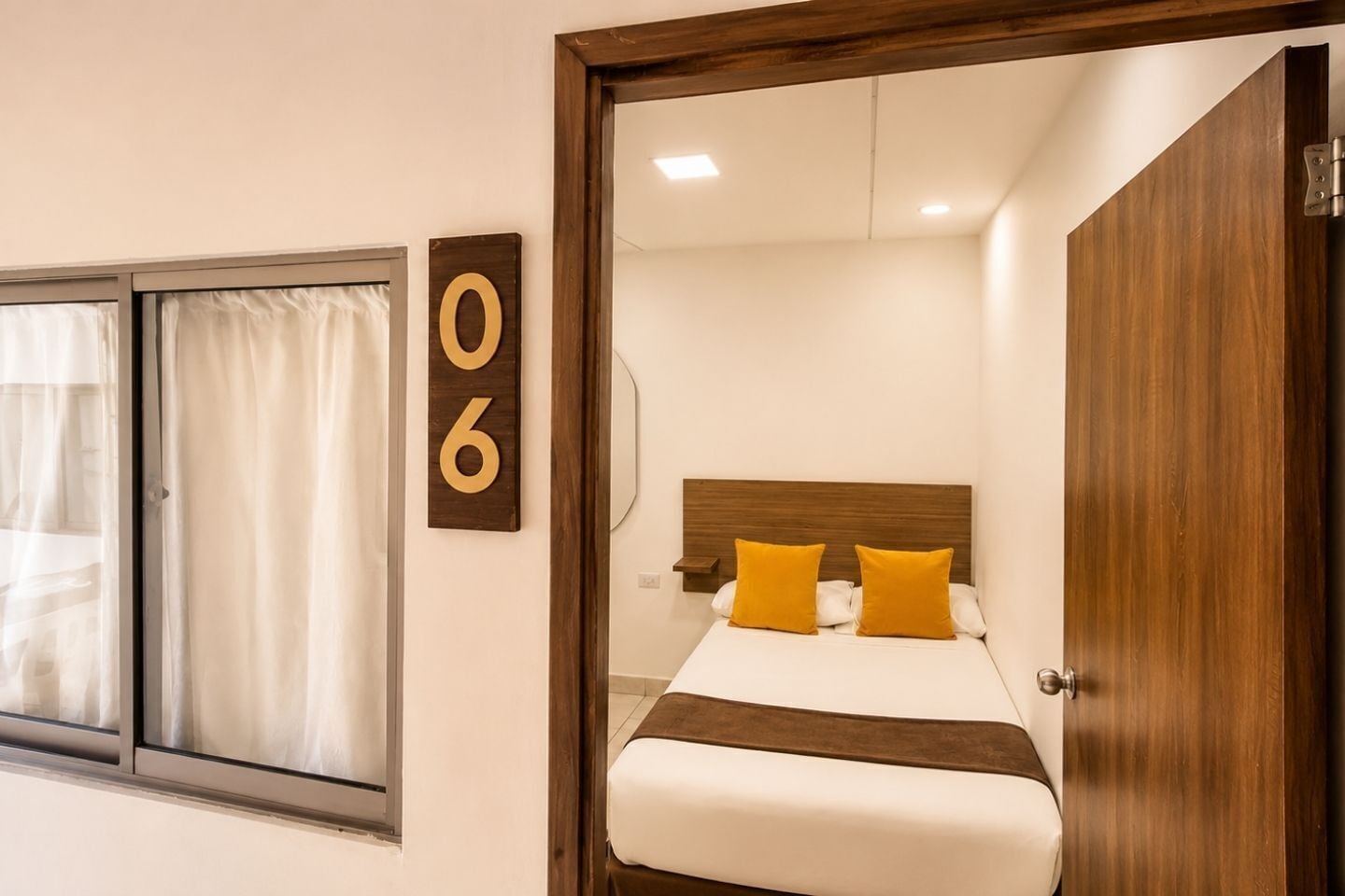 A hotel room with a bed, a wooden headboard, a window with curtains, and a door.