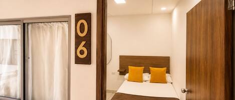 A hotel room with a bed, a wooden headboard, a window with curtains, and a door.