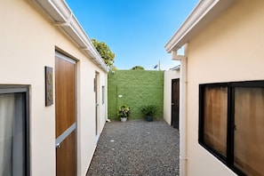 A narrow alleyway with a green textured wall, two potted plants, and a gravel path. - Ayenda Hotel Helenas (Riohacha)