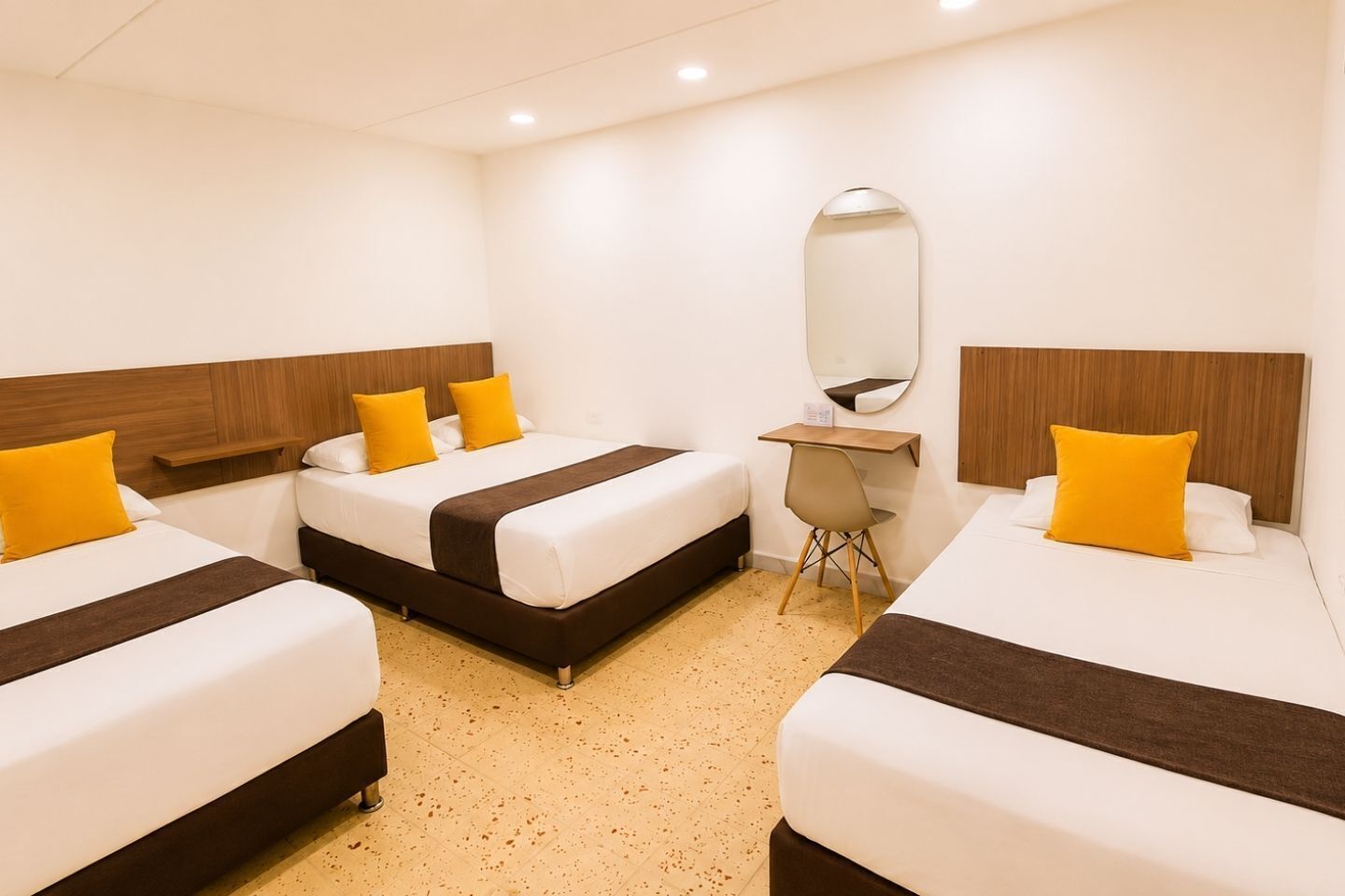 A hotel room with three beds, a desk, a chair, and a large mirror.