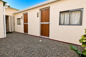 A building with numbered doors, a gravel courtyard, and a window with curtains. - Ayenda Hotel Helenas (Riohacha)