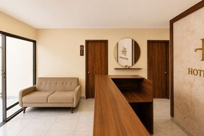 A hotel reception area with a sofa, a reception desk, a mirror with a sign, and two doors.