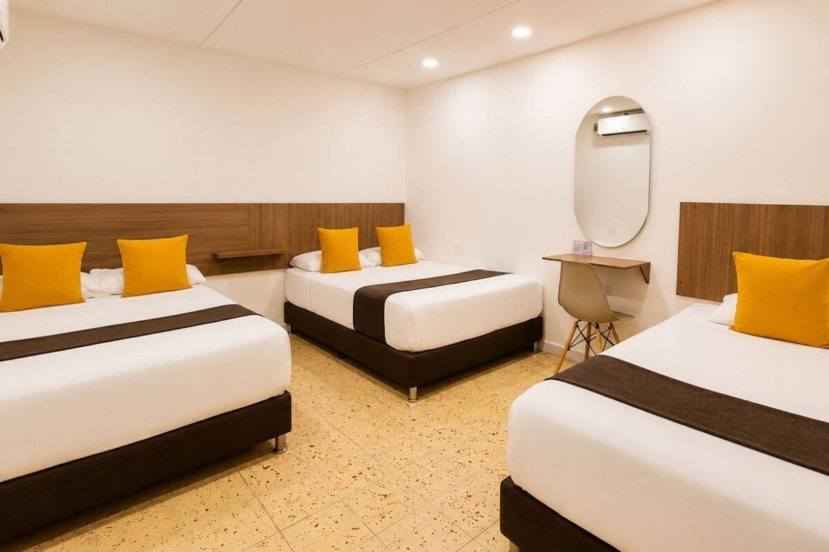 A hotel room with three beds, a desk, a chair, and a mirror.