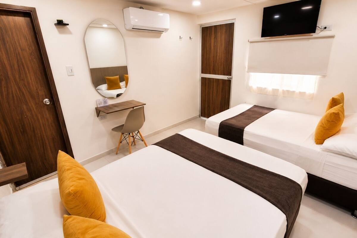 A hotel room with two beds, a desk, a chair, a TV, and a wardrobe.