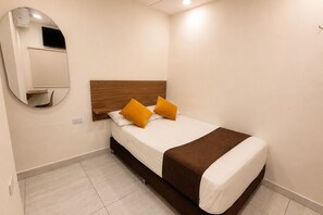 A hotel room with a bed, a mirror, a wooden headboard, and a brown throw blanket.