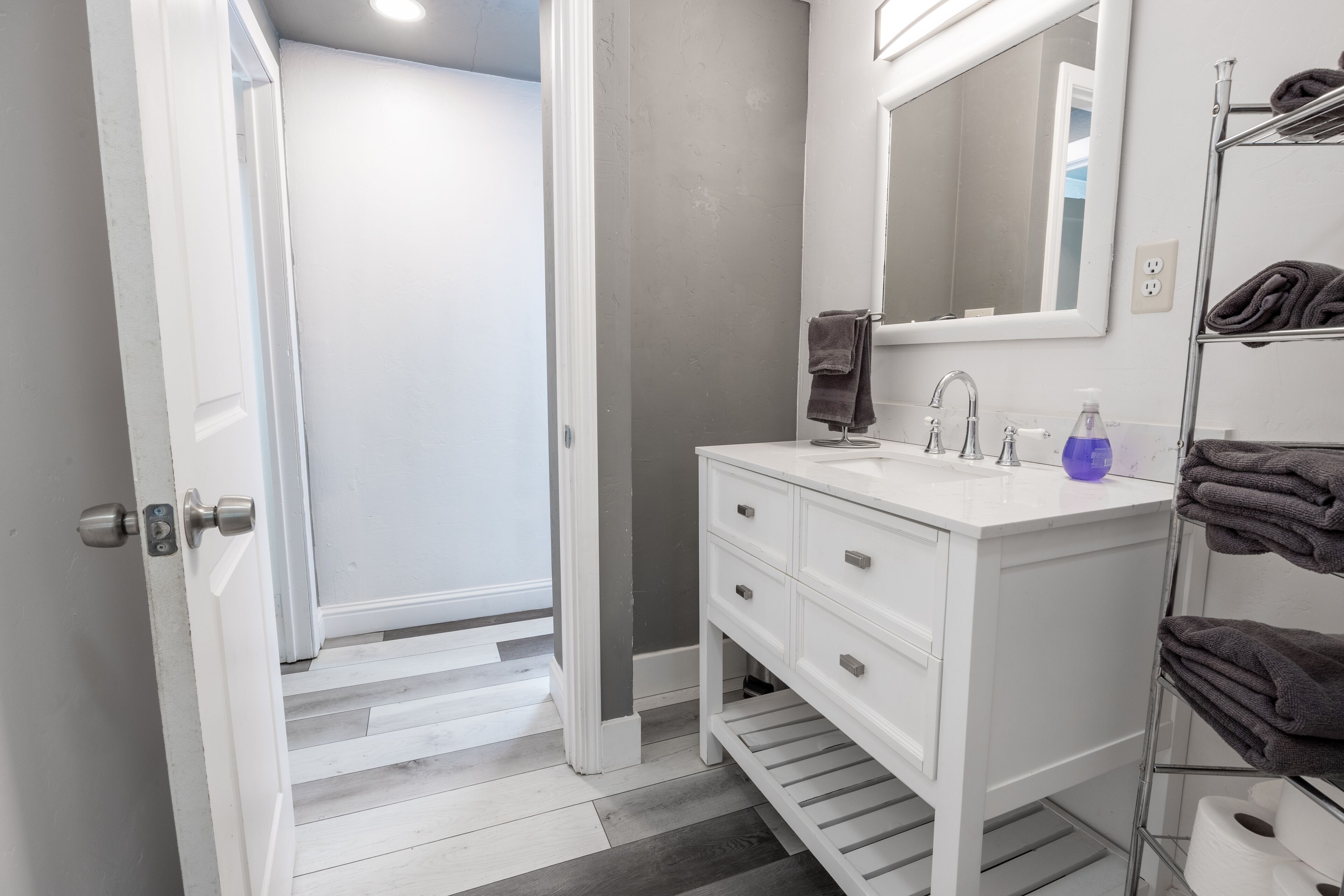 A bathroom with a white vanity, a mirror, a towel rack, and a striped floor.