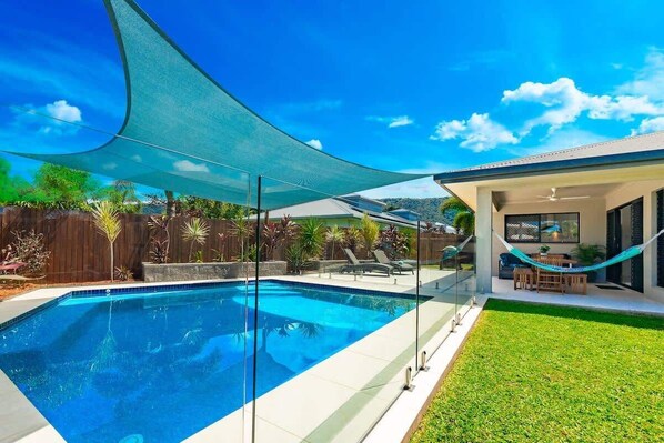A swimming pool with a glass enclosure, a hammock, and a patio area with outdoor furniture. - Tropical Dreams—Spacious Retreat with Private Pool (Smithfield)