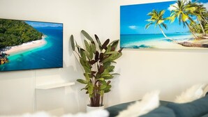 A room with a flat-screen TV, a potted plant, and two framed beach paintings on the wall. - Tropical Dreams—Spacious Retreat with Private Pool (Smithfield)
