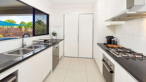 A modern kitchen with a gas stove, double sink, and a view of the outdoor area. - Tropical Dreams—Spacious Retreat with Private Pool (Smithfield)
