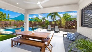 A patio with a pool, wooden table, and seating area. - Tropical Dreams—Spacious Retreat with Private Pool (Smithfield)