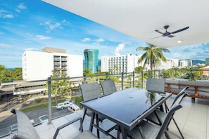 Un balcone con tavolo e sedie, una ventola a soffitto e vista sulla città.