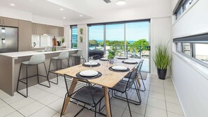 A modern kitchen with a dining area, large windows, and a view of the outdoors.