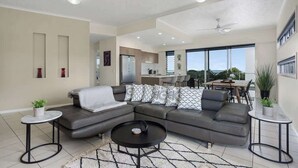 A modern living room with a sectional sofa, a round coffee table, and a dining area in the background.