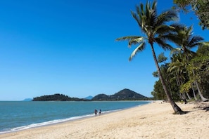 Una playa con palmeras, cielo despejado y una montaña a lo lejos.