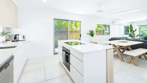 Una cucina moderna con isola centrale, zona pranzo con tavolo in legno e porta scorrevole in vetro che dà su un balcone.