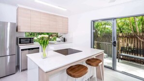 Una cucina moderna con un piano di lavoro bianco, elettrodomestici in acciaio inossidabile e un'ampia porta scorrevole in vetro che dà su un patio.