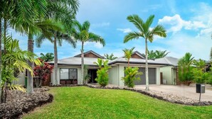A two-story house with a well-maintained lawn, palm trees, and a clear sky. - Tropical Pool Sanctuary in Kewarra Beach (Kewarra Beach)