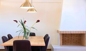 Et spiseområde med et træbord, sorte stole, en vase med blomster og en murstenspejs.
