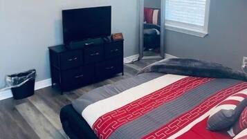 A bedroom with a bed, a dresser, a television, a window with blinds, and a ceiling fan.