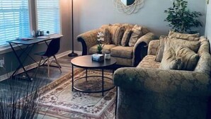 Un salon avec un canapé, une table basse, une lampe sur pied, un ventilateur de plafond et une plante en pot.