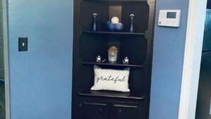 Un meuble d’angle avec des étagères, agrémenté d’objets décoratifs et d’un thermostat.