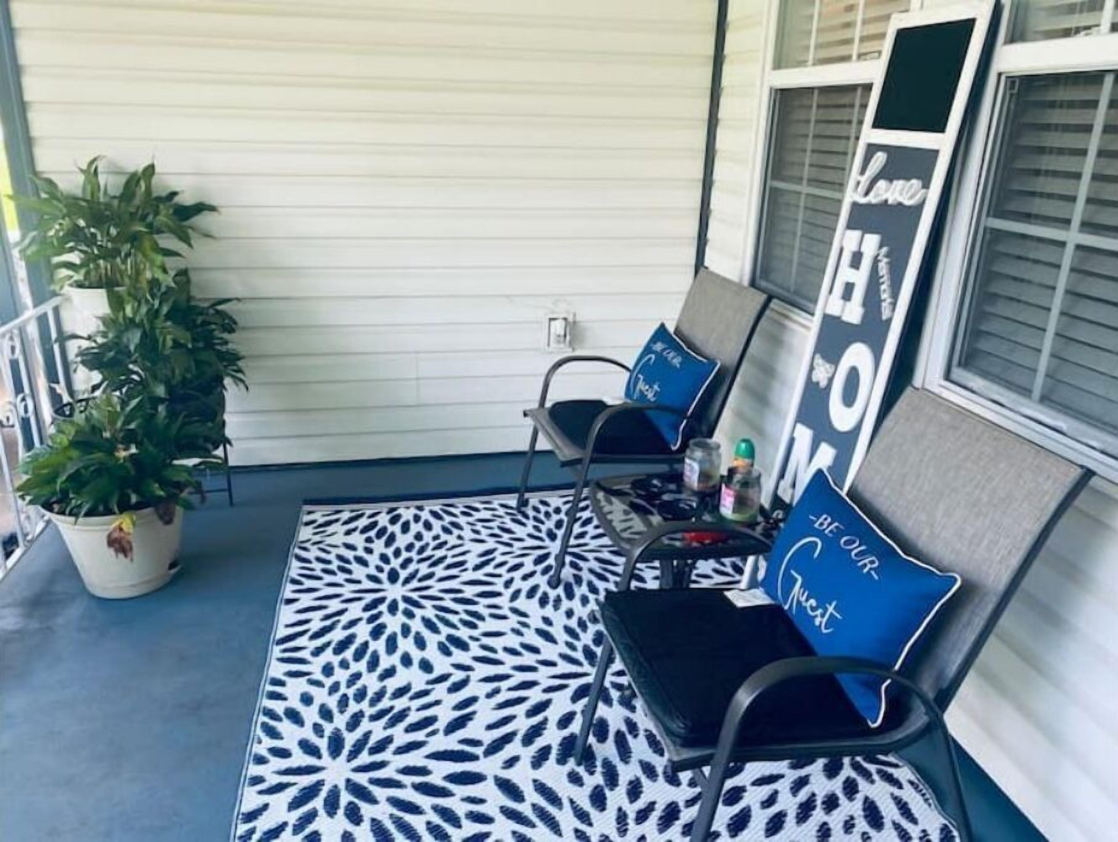 Een veranda met twee zwarte stoelen, een tapijt met een patroon, een potplant en een bordje met de tekst 'Love Home'.