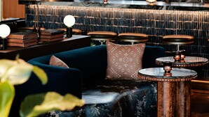 A cozy bar area with a high wooden ceiling, a large arched window, and a bar counter with various bottles. There are seating areas with cushioned sofas and round tables. - The Manchester  (Lexington)