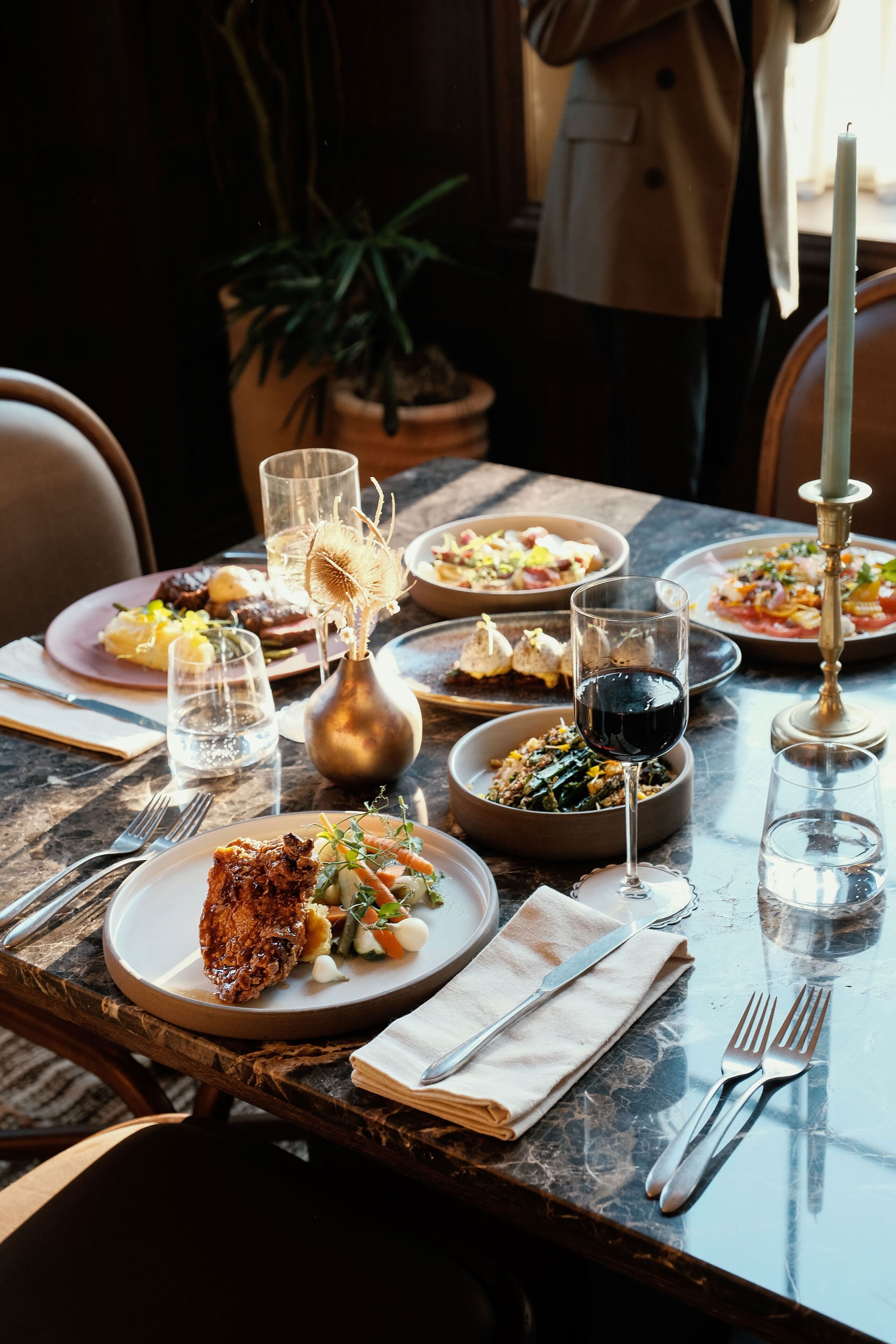 A dining table set with plates of food, glasses, and cutlery.