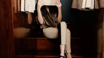 A person sitting on a wooden staircase, holding a book, with patterned curtains on either side.