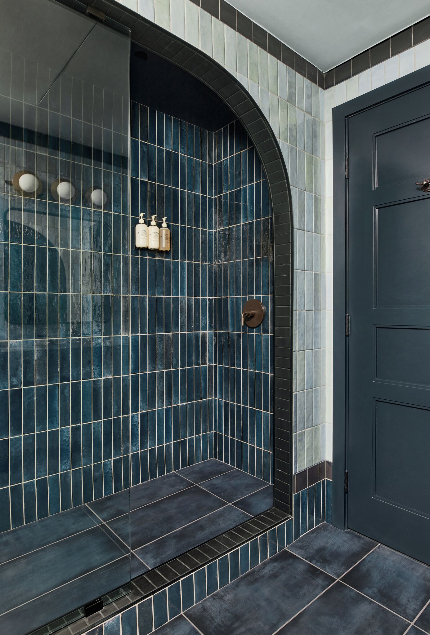 A bathroom with blue-tiled walls, a dark door, and a shower area.