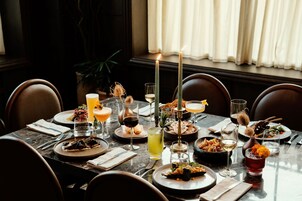 Mesa de jantar posta com diversos pratos, copos e velas, sugerindo uma experiência gastronômica requintada.