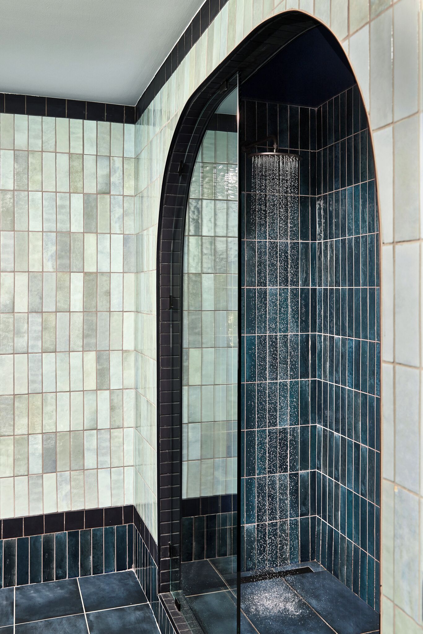 A tiled shower area with a curved arch and a vertical water feature.