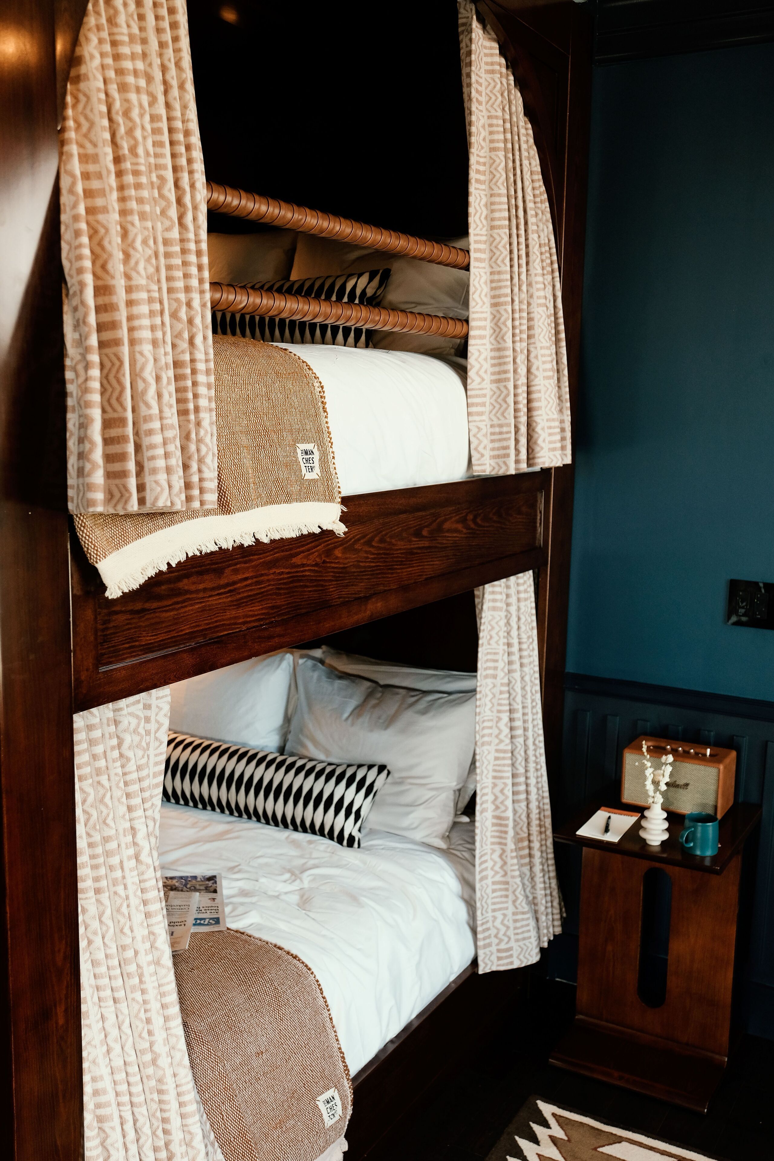 A bunk bed with patterned curtains and a small bedside table with a clock and a mug.
