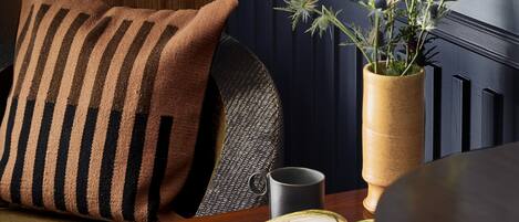 A cozy seating area with a striped pillow, a table with a magazine, a vase with flowers, and a wall-mounted lamp.