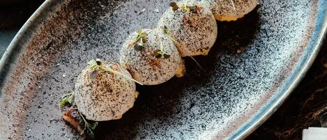 A plate with three spherical food items garnished with microgreens, placed on a textured ceramic plate.
