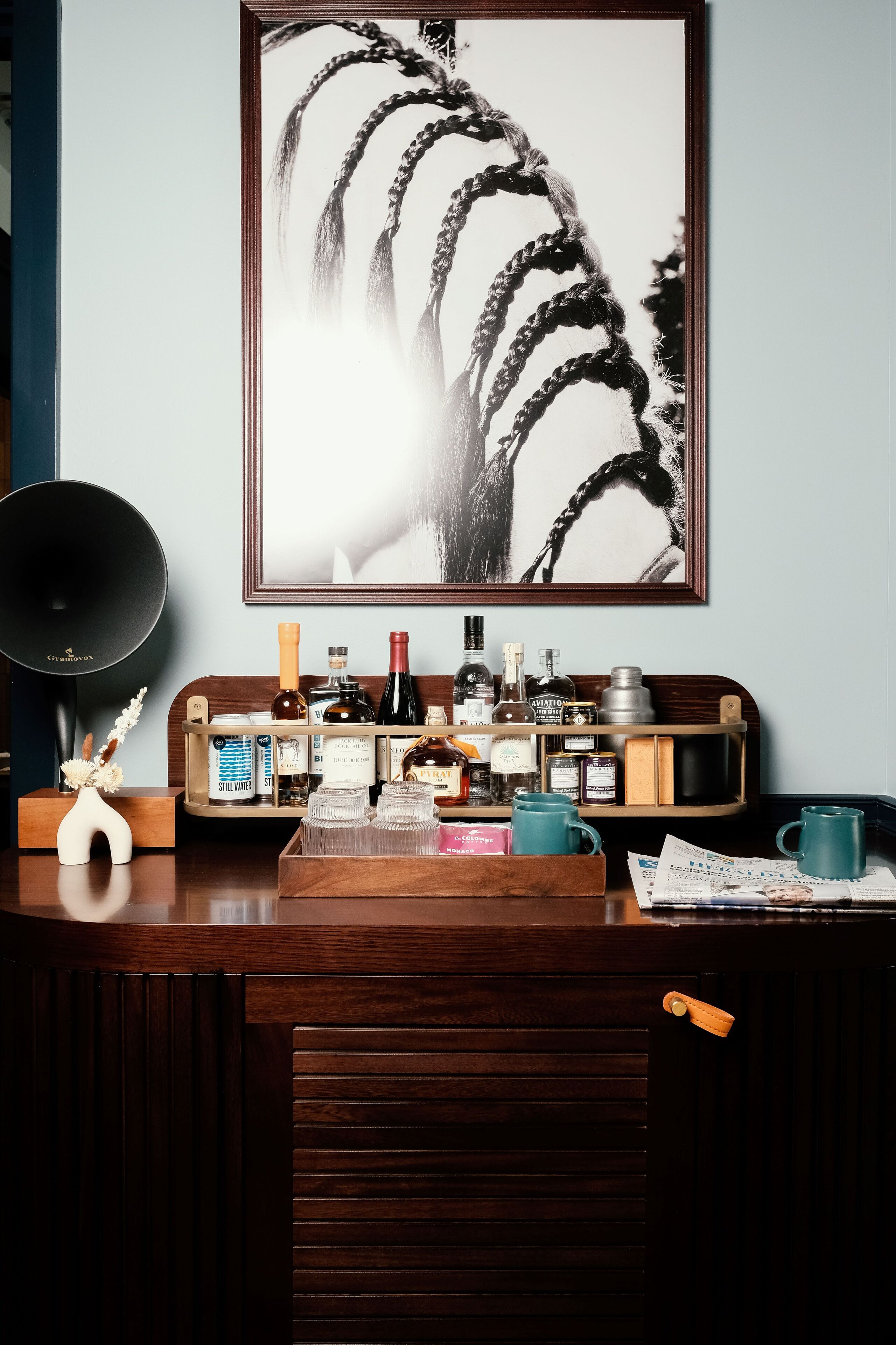 Un bureau en bois orné d’un tableau encadré, un haut-parleur noir et divers flacons et récipients.