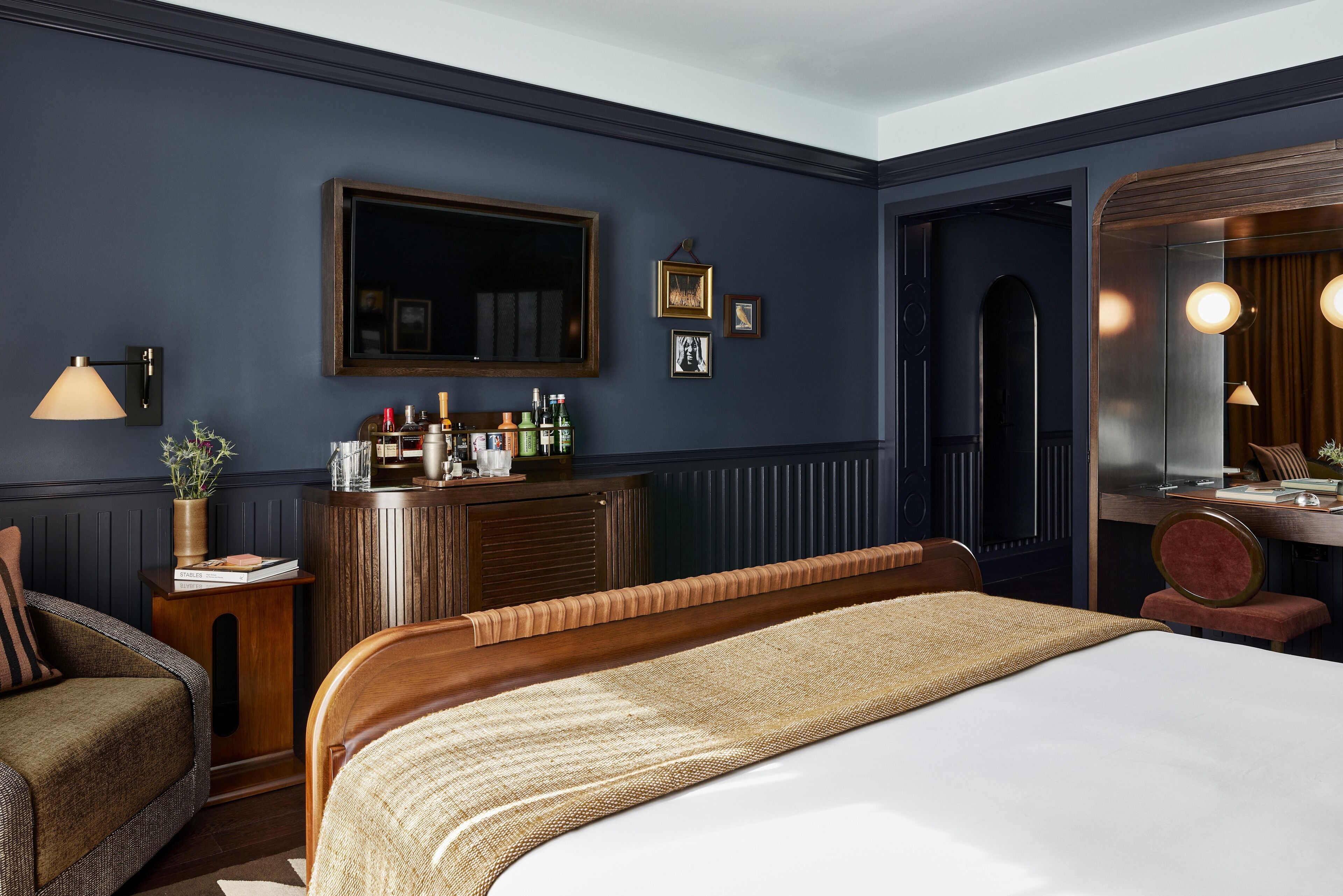 A hotel room with a large bed, a wooden dresser, a mirror, and a seating area with a chair and a small table.