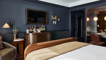 A hotel room with a large bed, a wooden dresser, a mirror, and a seating area with a chair and a small table.