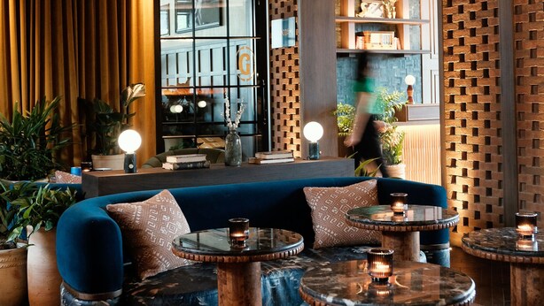 A cozy lounge area with a blue sofa, round coffee tables, and a wooden archway. - The Manchester  (Lexington)