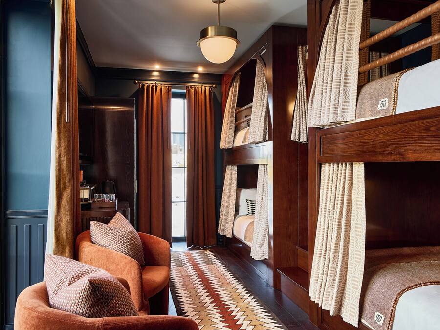 A room with a bunk bed, a sofa, a patterned rug, and curtains.