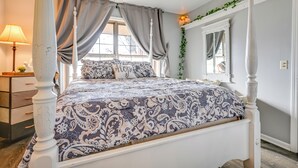 Un letto a baldacchino con copripiumino decorato, un comodino con lampada e una finestra con tende.