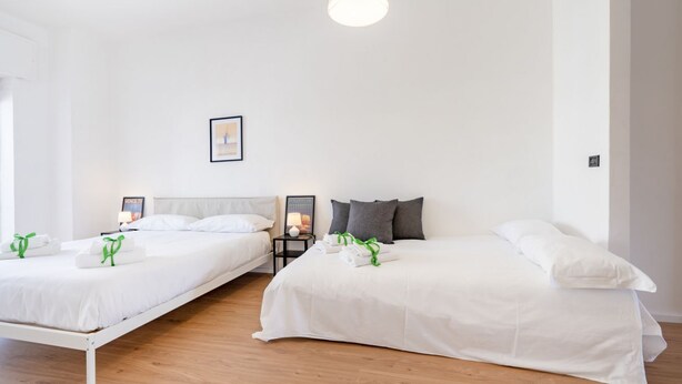 Ein Hotelzimmer mit zwei Betten, weißer Bettwäsche, einem gerahmten Bild an der Wand und einem Nachttisch mit einer Lampe.