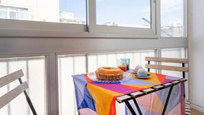 Ein Tisch mit farbenfroher Tischdecke, Kuchen und einem Glas Saft in einem Zimmer mit großen Fenstern.